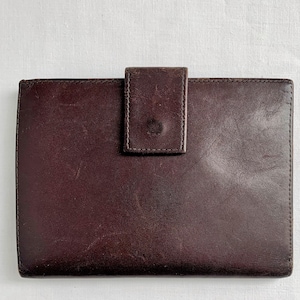 May include: A dark brown leather wallet with a flap closure. The wallet has a smooth, worn texture.