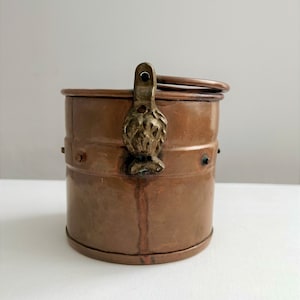 May include: A small copper container with a hinged lid and a decorative brass handle. The container has a worn, aged look and is likely antique.