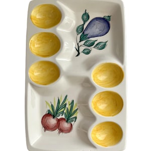 May include: Rectangular white ceramic serving platter with eight yellow-painted egg indentations. The platter features hand-painted illustrations of an eggplant, red onions, and green leaves. A decorative and functional piece for serving appetizers or snacks.