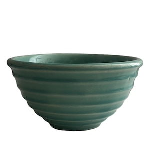 May include: A teal-colored ceramic bowl with a ribbed exterior. The bowl has a rounded shape with a slightly flared rim. The teal color is consistent throughout the bowl, and the surface appears smooth and glossy.