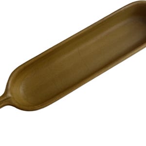 May include: A long, wooden serving dish with a handle. The dish is a light brown color and has a smooth, polished finish.
