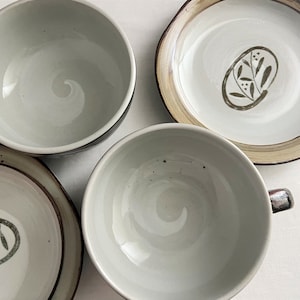 May include: Set of four white ceramic bowls with brown trim. The bowls have a simple design with a leafy motif.