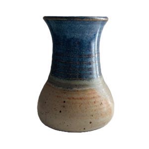 May include: A handcrafted ceramic vase with a flared top and a rounded base. The vase features a gradient of colors, transitioning from a deep blue at the top to a beige and tan base. The vase has a textured surface and is suitable for home decor.