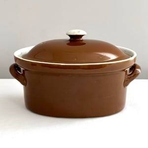 May include: A brown ceramic casserole dish with a lid and two handles. The lid has a white knob.