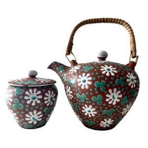 May include: A brown ceramic teapot and sugar bowl set with a white and green floral design. The teapot has a woven wicker handle.