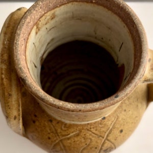 May include: A brown ceramic vase with a wide mouth and a handle. The vase has a textured surface and a brown glaze.