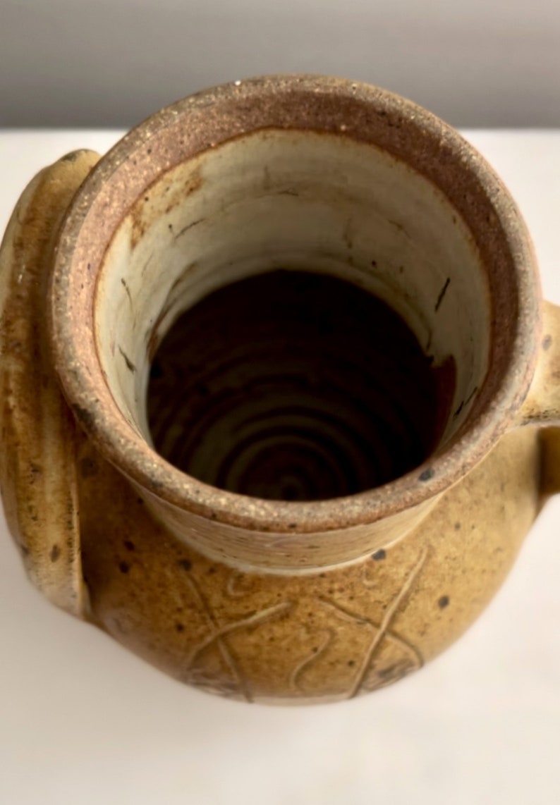 May include: A brown ceramic vase with a wide mouth and a handle. The vase has a textured surface and a brown glaze.
