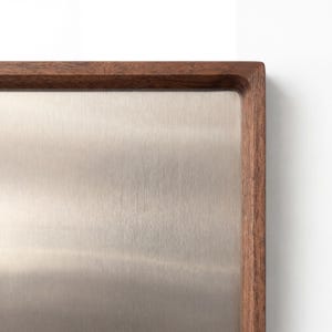 Close-up of the upper right corner of the walnut wood frame and brushed metal surface of the magnetic board.