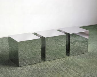 May include: Three identical cube-shaped stools with a highly reflective, polished chrome mirror finish. Each piece features sharp, clean edges and a square top surface, creating a uniform geometric appearance across all three individual units.
