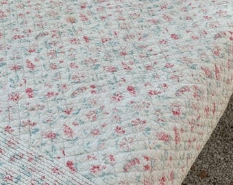 Può includere: Un copriletto trapuntato bianco con un motivo floreale ripetuto nei toni del rosa e dell'azzurro. Il tessuto presenta una texture trapuntata a rombi su tutta la superficie, con un distinto bordo orizzontale a coste lungo il margine inferiore.