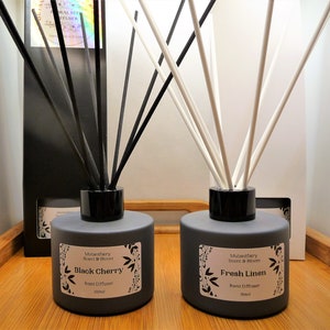 May include: Two grey glass reed diffusers with black lids and black and white reeds. The diffuser on the left is labelled "Black Cherry" and the diffuser on the right is labelled "Fresh Linen". Both diffusers are 100 ml.