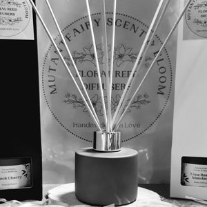 May include: A brown glass diffuser bottle with a silver lid and white sticks. The bottle is labelled "Mutant Fairy Scent & Bloom Floral Reed Diffuser" and "Handmade with Love".