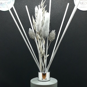 May include: A grey diffuser bottle with a silver cap and white reeds. The reeds are topped with dried grasses and flowers.