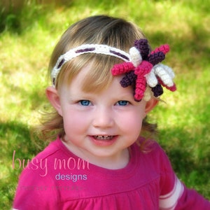 May include: A young girl wearing a pink shirt with white stripes and the text "Daddy's MVP" on the front. She is wearing a white and purple crocheted headband with a flower design.