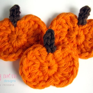 Peut inclure: Trois citrouilles orange en crochet avec des tiges brunes. Les citrouilles sont disposées en grappe sur un fond blanc.