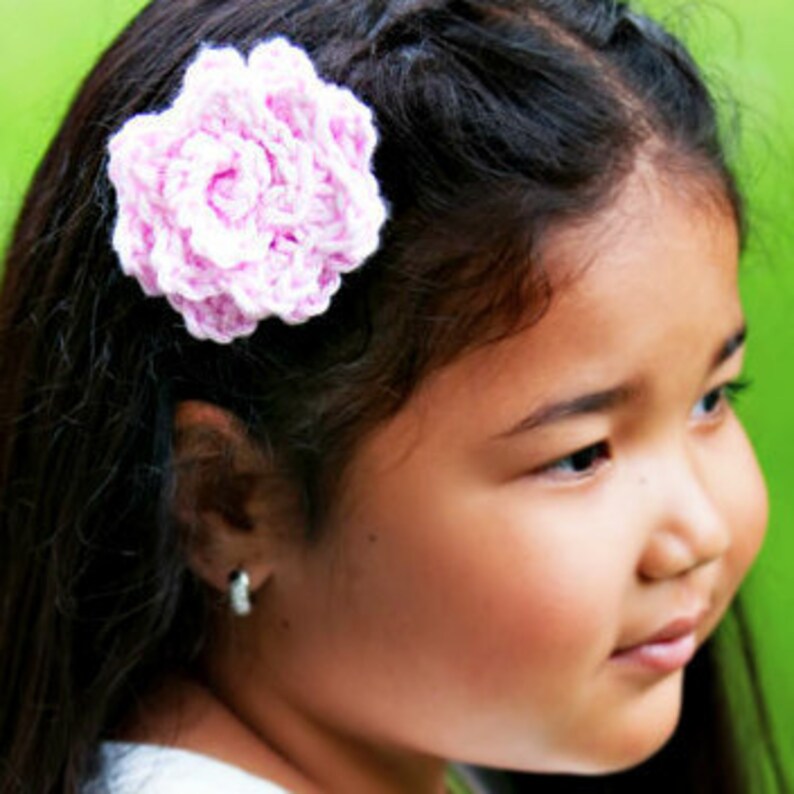 May include: A pink crocheted flower hair clip. The flower is about 2 inches in diameter and has a ruffled edge.