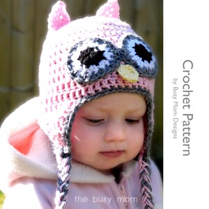 May include: A pink and gray crocheted owl hat with a yellow beak and black eyes. The hat has long ties that are braided. The hat is on a child's head.