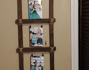 May include: A rustic wooden picture frame with three openings for photos. The frame is made of dark brown wood and has a rope running through it. The frame is hanging on a wall and has three photos in it.