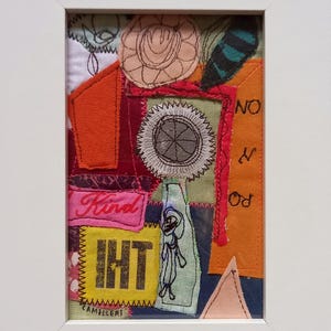 May include: A framed textile collage featuring layered fabric scraps in orange, pink, yellow, and blue. The piece includes embroidered details, a circular stitched motif, and the text "Kind", "IHT", "NO", "N", "RO", and "CAMILLERI" stitched onto the fabric.