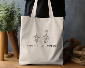 Può includere: Borsa tote in tela bianca con testo nero e illustrazioni. Il testo recita "With faith of a mustard seed". Le illustrazioni sono due piante con radici e un solo fiore.