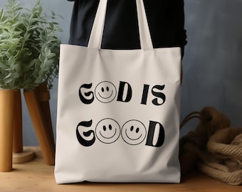 Può includere: Borsa tote in tela bianca con testo nero e faccine sorridenti che recita "Dio è buono".
