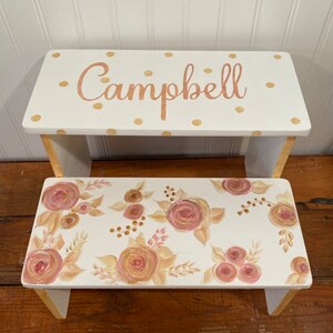 May include: White wooden step stool with a gold polka dot top and the name "Campbell" written in gold. The bottom step has a floral design with pink and brown roses.