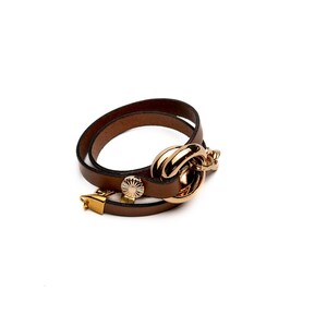 May include: A brown leather wrap bracelet with a gold-tone clasp and decorative accents. The bracelet features a double-wrap design and a large, gold-tone circular clasp. The bracelet is approximately 7 inches in length.