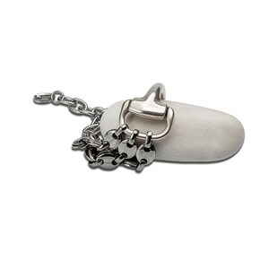 May include: A silver metal chain and hardware are attached to a smooth, white stone. The chain is draped over the stone, and the hardware includes a large ring and several smaller, decorative links. The background is plain white.