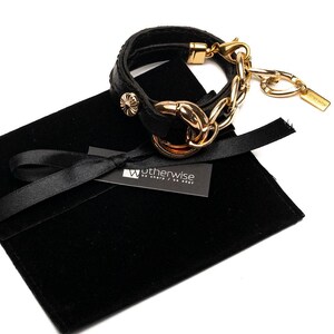 Puede incluir: Pulsera de cuero negro con cadena y herrajes dorados. La pulsera tiene un dise&ntilde;o de doble vuelta con un cierre dorado decorativo y una peque&ntilde;a etiqueta. Presentada en una bolsa de terciopelo negro con una etiqueta "Wotherwise be sharp / be edgy."