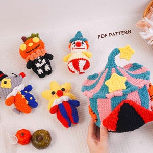 May include: A collection of crocheted items including a circus tent container, a mouse, a pumpkin figure, a clown, and a star-shaped character. The text PDF PATTERN is visible. The items feature vibrant colors like orange, blue, pink, and yellow.