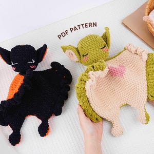 Peut inclure: Deux peluches crochetées sont présentées, l'une noire avec des détails orange et l'autre verte et beige. Le jouet vert présente un cœur rose. Le texte "PDF PATTERN" est visible sur l'image.