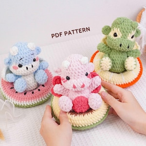 May include: Three handmade crochet cow plushies in blue, pink, and green, each sitting on a crocheted fruit slice. The blue cow is on a watermelon slice, the pink cow on an avocado slice, and the green cow on an orange slice. The text "PDF PATTERN" is visible.