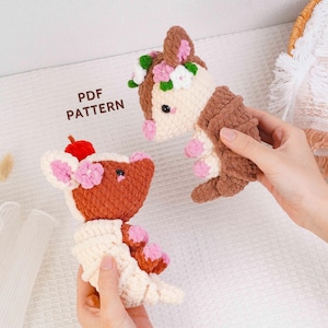 Puede incluir: Dos muñecos de animales de ganchillo hechos a mano. Uno es marrón y crema con detalles florales rosas y blancos y una cereza roja. El otro es marrón y crema con detalles florales rosas y verdes. El texto "PDF PATTERN" es visible.