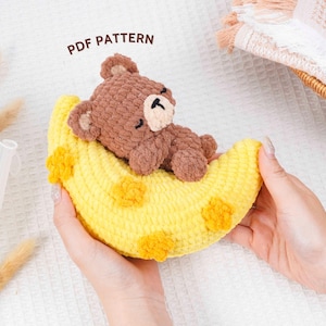Könnte beinhalten: Ein handgefertigter Häkelbär liegt auf einem gelben Halbmond. Der Bär ist braun mit einer hellbraunen Schnauze und schwarzen Augen. Der Mond hat gelbe und orangefarbene Akzente. Der Text "PDF PATTERN" ist sichtbar.