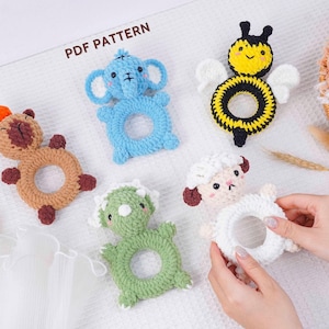 May include: A collection of handmade crochet baby toys in various animal shapes, including an elephant, bee, sheep, dinosaur, and a bear. The toys are in shades of blue, yellow, white, green, and brown. The text "PDF PATTERN" is visible.