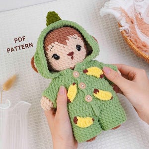 May include: A handmade crochet monkey doll wearing a green hooded jacket with yellow banana appliqués. The doll has brown fur, a light brown face, and button closures. The text "PDF PATTERN" is visible.