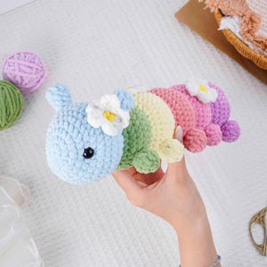 Puede incluir: Un juguete de oruga de ganchillo hecho a mano y colorido. La oruga est&aacute; hecha de hilo suave y afelpado en tonos de azul, verde, amarillo, rosa y morado. Cada segmento est&aacute; adornado con una flor blanca con centro amarillo. Un juguete caprichoso.