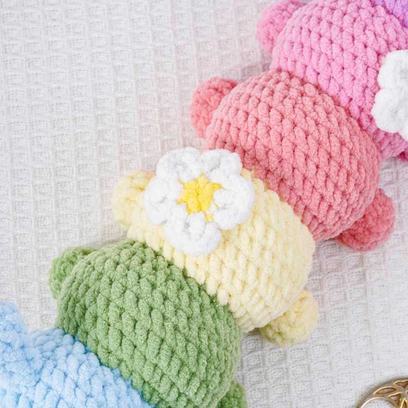 Puede incluir: Primer plano de varios osos de ganchillo hechos a mano en varios colores pastel. Cada oso tiene una flor unida a su cabeza. Los osos son en tonos de rosa, amarillo, verde y azul. El ganchillo tiene un aspecto texturizado.