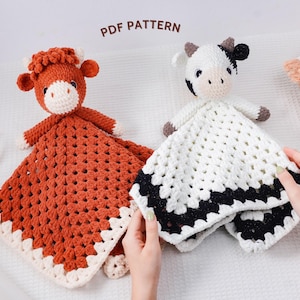 Könnte beinhalten: Zwei gehäkelte Kuh-Sicherheitsdecken. Eine ist rostfarben mit einem weißen und rostfarbenen Rand, die andere ist weiß mit einem schwarz-weißen Rand. Jede hat einen Kuhkopf mit Hörnern. Der Text "PDF PATTERN" ist sichtbar.