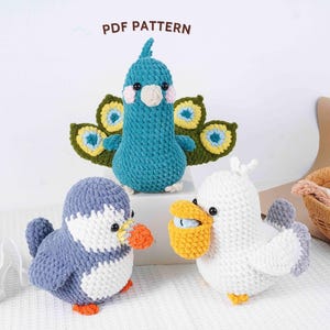 May include: Three handmade crochet bird figures: a blue peacock, a penguin, and a pelican. The peacock has a fan-shaped tail. The penguin is blue and white with an orange beak and feet. The pelican is white with a yellow pouch. The text "PDF PATTERN" is at the top.