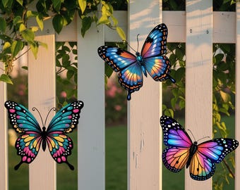 May include: Three decorative butterflies with detailed wing patterns are shown against a white picket fence. The butterflies display vibrant colours including blue, pink, yellow, and orange, adding a cheerful touch to the outdoor setting.