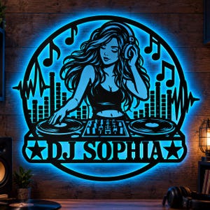 Puede incluir: Un letrero de pared circular con la silueta negra de un DJ con cabello largo y auriculares, detrás de una mesa de mezclas con tocadiscos y notas musicales, iluminado por una luz LED azul brillante, con el texto DJ SOPHIA.