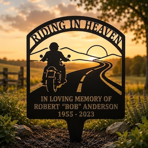 May include: A black metal memorial garden stake featuring a silhouette of a motorcyclist on a road with the text RIDING IN HEAVEN at the top and IN LOVING MEMORY OF ROBERT BOB ANDERSON 1955-2023 engraved at the bottom of the rectangular sign.