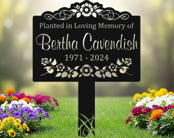Puede incluir: Una estaca de jardín conmemorativa de metal negro con el texto "Planted in Loving Memory of Bertha Cavendish 1971-2024". El letrero tiene adornos florales y está colocado en un jardín con flores coloridas.