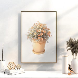 May include: A framed watercolor print of a potted plant with peach and yellow flowers. The pot is a light peach color and sits on a matching saucer. The artwork is displayed on a white wall, with decorative items in the foreground.