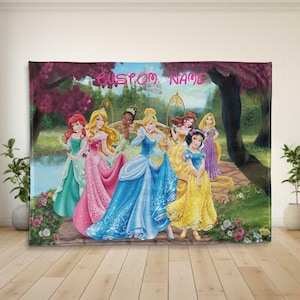 Puede incluir: Una manta rectangular grande con un grupo de princesas animadas con vestidos coloridos. Las princesas est&aacute;n situadas frente a un jard&iacute;n con un castillo a lo lejos. El texto "CUSTOM NAME" est&aacute; escrito en la parte superior.