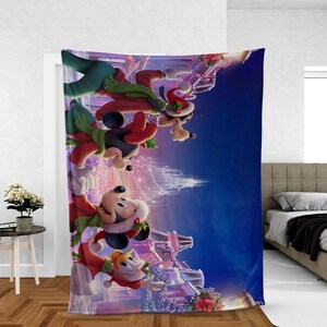 May include: A large, rectangular blanket featuring a festive scene with Disney characters. Mickey Mouse, Minnie Mouse, Goofy, and Donald Duck are depicted in holiday attire, with a backdrop of a winter wonderland and twinkling lights. The blanket is primarily blue, red, and white.