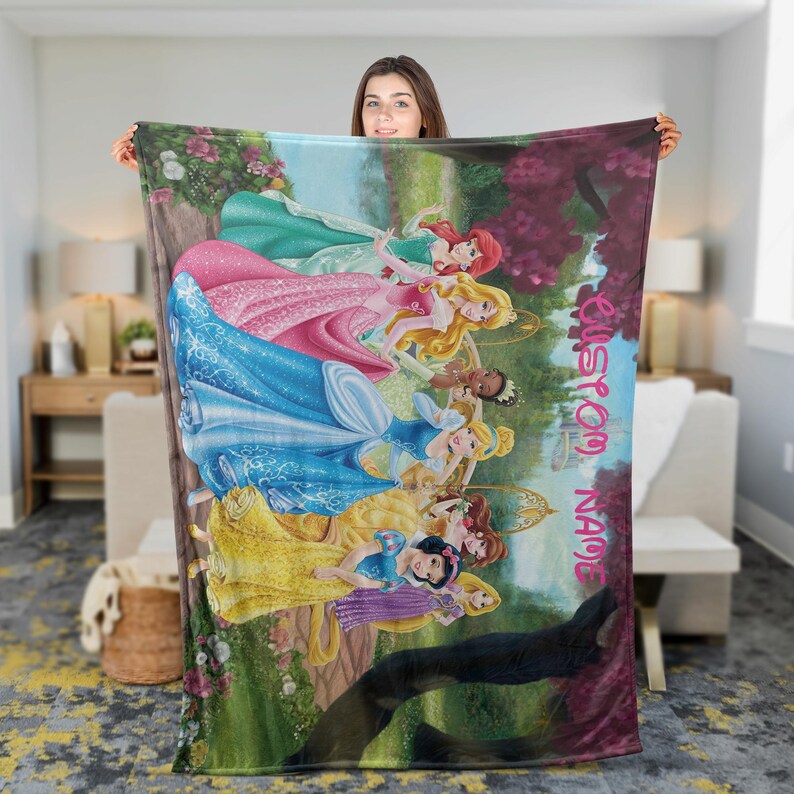 Puede incluir: Una manta personalizada con una colorida ilustraci&oacute;n de princesas con sus vestidos. La manta tiene un fondo verde, rosa y azul con el texto "CUSTOM NAME" en escritura vertical.