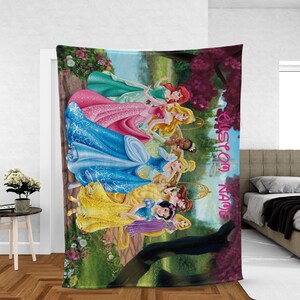 Puede incluir: Una colorida manta con ilustraciones de varias princesas con sus vestidos ic&oacute;nicos. La manta tiene una combinaci&oacute;n de colores verde, rosa y azul con las palabras "CUSTOM NAME" en escritura rosa. Las princesas est&aacute;n ambientadas en un fondo de bosque.