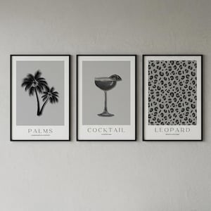 May include: Three framed art prints with black frames. The prints feature a palm tree silhouette, a cocktail illustration, and a leopard print pattern. Each print has a gray background and white text at the bottom.